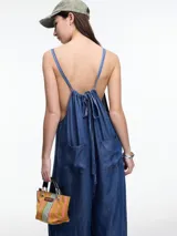 Mono largo de denim azul oscuro, con breteles finos regulables, escote recto, bolsillos traseros y corte amplio de pierna recta.