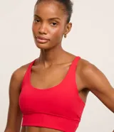 Top deportivo alargado color rojo, confeccionado en microfibra con escote en U, tiras finas cruzadas en la espalda y cintura ancha. Incluye copas removibles.
