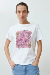 Remera blanca de algodón con estampado de flores rosadas y texto 'LET LOVE IN'.
