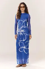 Vestido largo de malla azul traslúcida con estampado de flores blancas, cuello alto y mangas largas. Tiene aberturas laterales en el ruedo.