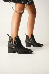 Botas texanas cortas de cuero color marrón con puntera metálica, detalles de tachas y arnés con hebilla. Taco de madera.