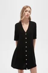 Vestido corto negro de algodón, corte holgado, con cuello en V y cierre frontal con botones.