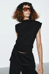 Top de algodón color beige, con cuello recto, mangas asimétricas y detalle de tejido drapeado en el lateral.