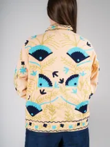 Chaqueta color crema con bordados de flores y figuras geométricas en tonos azul, celeste y dorado.