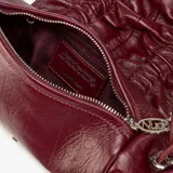 Bolso pequeño tipo clutch o bandolera de cuero color bordó, con efecto arrugado y fruncido en la parte superior y cordones ajustables con herrajes metálicos plateados. Posee una correa larga y fina para llevar al hombro.