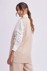 Chaleco largo color beige con solapas, cierre con dos botones y bolsillos delanteros.