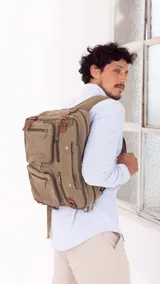 Mochila de tela canvas color beige con detalles en cuero marrón. Cuenta con múltiples bolsillos con cierre, compartimento acolchado para notebook y correas ajustables.