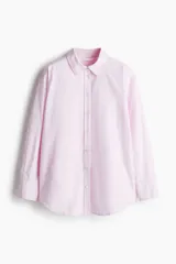 Camisa rosa de algodón Oxford con cuello clásico, botones al frente, canesú con trabilla en la espalda, corte relajado, hombros caídos, mangas largas con puños sencillos, bolsillos superiores con solapa y bajo redondeado con espalda más larga.