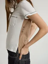 Remera blanca con bolsillo en el pecho y detalle bordado. Corte recto y mangas cortas con terminación desflecada. Panel lateral color beige con inscripción vertical.