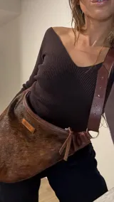Cartera bandolera de cuero con pelo animal print marrón y blanco, correa de cuero ajustable con hebilla y cierre con cremallera.