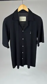 Camisa negra tejida de algodón con cuello solapa, manga corta y cierre frontal con botones.