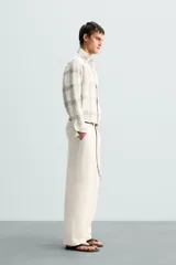 Pantalón color crema de lino, corte relaxed fit, con pliegues frontales, bolsillos laterales y traseros de vivo.