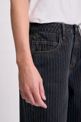 Pantalón de jean negro con rayas verticales blancas, corte recto y tiro alto.