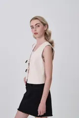 Chaleco sin mangas color marrón oscuro, de corte ajustado al cuerpo, con escote en V y cierre frontal mediante lazos anudados con detalles de cuentas oscuras.