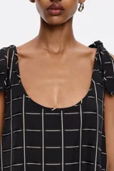 Vestido midi negro con estampado a cuadros blancos, corte recto, escote redondo y tirantes con lazos.
