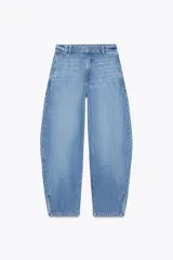 Pantalón de jean celeste de tiro medio, corte amplio tipo globo, con bolsillos delanteros y traseros, trabillas en la cintura, abertura lateral en el ruedo y cierre frontal con cremallera y botón.