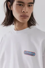 Remera blanca de algodón pesado con cuello redondo ribeteado, hombros caídos, bajo recto y estampado pequeño en el pecho. Corte oversized.