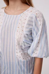 Blusa blanca con rayas verticales celestes, mangas abullonadas y detalles de calado en los hombros y el frente.