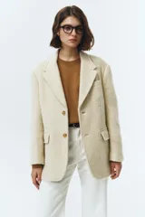 Blazer de lana con mezcla de alpaca en color beige, con cuello sastre, cierre frontal de dos botones y bolsillos laterales con solapa. Presenta una textura suave y vellosa.