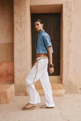 Camisa de denim celeste de corte crop, con cuello solapa, escote en pico, manga corta y dos bolsillos delanteros con botón. Cierre frontal con botones metálicos.