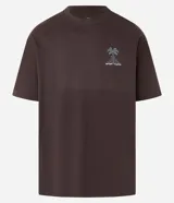 Remera marrón de corte relajado, confeccionada en algodón. Presenta cuello redondo, mangas cortas y estampa frontal y trasera de palmeras con la leyenda 'Work Hard'.