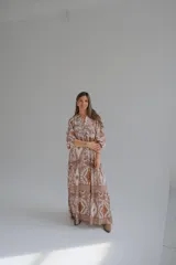 Vestido largo color rosa con estampado floral y geométrico en tonos blanco y naranja. Tiene cuello mao, mangas 3/4 y corte escalonado en la falda.