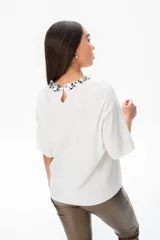 Remera blanca de viscosa con cuello redondo decorado con apliques plateados y mangas cortas amplias.