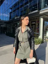 Vestido camisero corto color verde con textura arrugada, manga larga, cuello camisero, cierre frontal con botones, cinturón negro con hebilla dorada y bolsillos con solapa en el pecho.