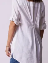 Camisola larga de algodón color blanco, marca Dash. Tiene cuello con solapa, abertura central con botones, bolsillo aplicado en el pecho, mangas regulables con presilla y botón, y bolsillos laterales en la costura.