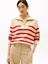 Sweater de punto color crema con rayas horizontales rojas, cuello alto con cremallera metálica y logo de Tommy Hilfiger bordado en el pecho.