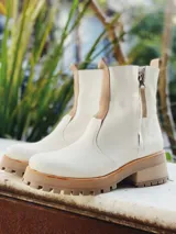 Botas de cuero color blanco hueso, con elástico lateral color beige y cierre lateral con cremallera. Suela track color beige.