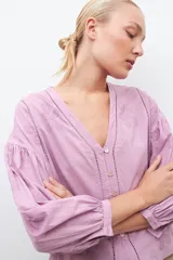 Blusa lila con bordados, de mangas largas abullonadas y cuello en V.
