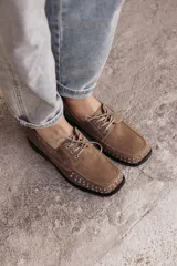 Mocasín de cuero color marrón claro con tachas metálicas plateadas en la puntera y laterales.