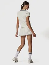 Polera manga corta color blanco tiza, con cuello polo y escote en V. Presenta dos rayas azules en el cuello y un logo bordado en negro en el pecho.