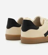Championes estilo chutera color crema con detalles laterales y traseros en negro. Suela plana color caramelo y cierre con cordones. Confeccionados en poliuretano y poliéster.