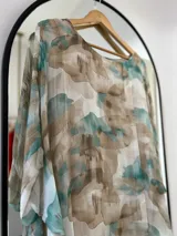Blusa de seda italiana con estampado abstracto en tonos aqua, marrón y blanco. Tiene cuello redondo y corte asimétrico en el ruedo. Incluye musculosa interior.