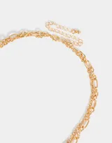 Collar corto dorado de doble cadena, una de eslabones y otra de perlas sintéticas. Incluye dijes de cruz, bota cowboy, moneda antigua y otros.