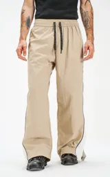 Pantalón deportivo beige de nylon con cintura elástica ajustable con cordón, corte amplio y aberturas laterales con broches.