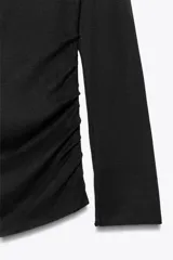 Camiseta negra de algodón con escote recto, hombros descubiertos y mangas largas. Presenta detalle de frunces en el frente.