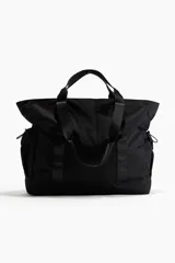 Bolso de deporte negro de tela impermeable con doble asa de mano y correa de hombro ajustable. Tiene bolsillos laterales con cordón elástico y dos compartimentos interiores, uno con cierre y otro de malla.