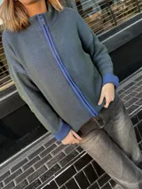 Campera tejida color gris con textura vanizada, cierre frontal con cremallera azul y cuello alto.