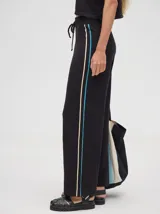 Pantalón negro de algodón, corte holgado y pierna ancha con pretina elástica. Presenta rayas blancas y celestes a los costados.