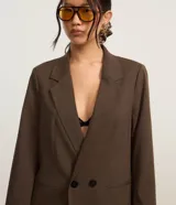 Blazer marrón de poliéster y viscosa, de corte amplio y estructura de sastrería, con solapas en el cuello, doble abotonadura, bolsillos falsos y pinzas.