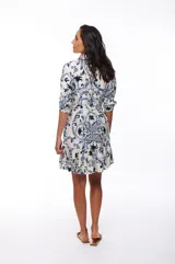 Vestido corto con estampado floral en tonos azules y negros sobre fondo blanco, corte camisero con cuello clásico, mangas 3/4 y falda con volantes.