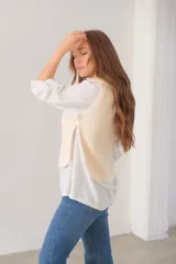 Chaleco corto de punto color crudo, con cuello alto, medio cierre frontal y botones laterales.