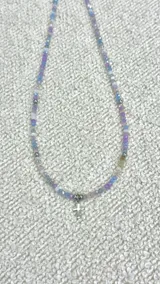Collar de cristalitos facetados en tonos lila, celeste y plateado, con dije de cruz en acero plateado. Cierre de acero.