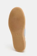 Zapatillas deportivas blancas con detalles en celeste y suela color caramelo.