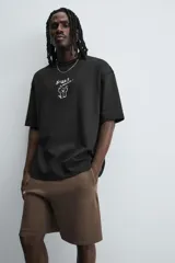 Camiseta negra de corte relaxed fit, cuello redondo y manga corta. Estampado frontal con dibujo de gato y texto en japonés.