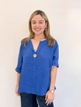 Blusa azul de lino con cuello en V y manga 3/4. Tiene un botón de madera decorativo en el centro del escote.