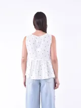 Blusa blanca sin mangas con escote en V y cierre frontal con botones.